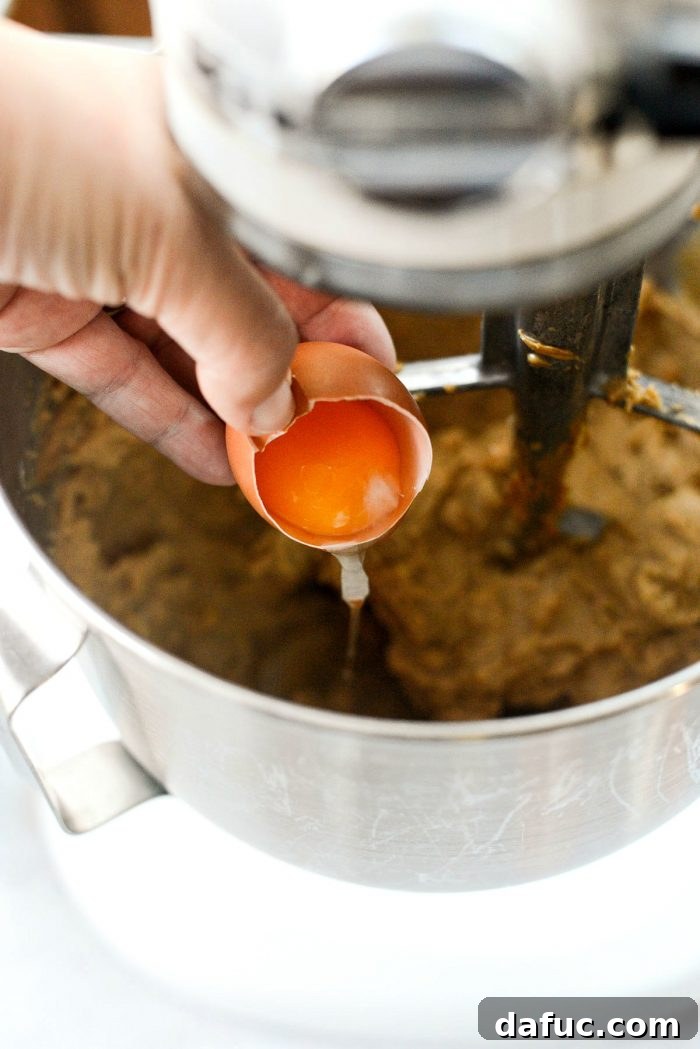 Adding eggs one at a time to the cookie dough mixture