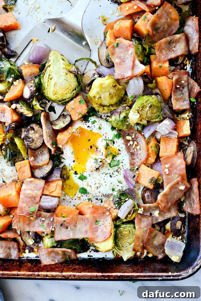 Sheet Pan Breakfast Hash: A vibrant medley of roasted Brussels sprouts, sweet potatoes, mushrooms, onion, and bacon, topped with baked eggs, all cooked on one pan for an easy and healthy breakfast. SimplyScratch.com recipe.