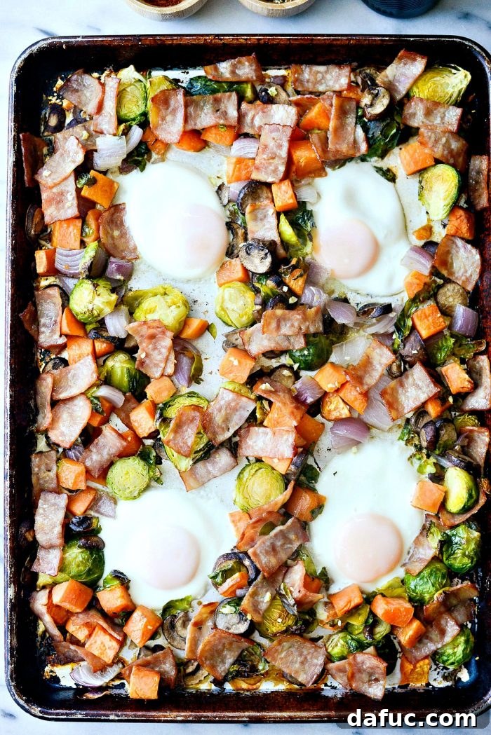 Close-up of the perfectly baked eggs with jammy yolks nestled in the sheet pan breakfast hash, ready to be served.