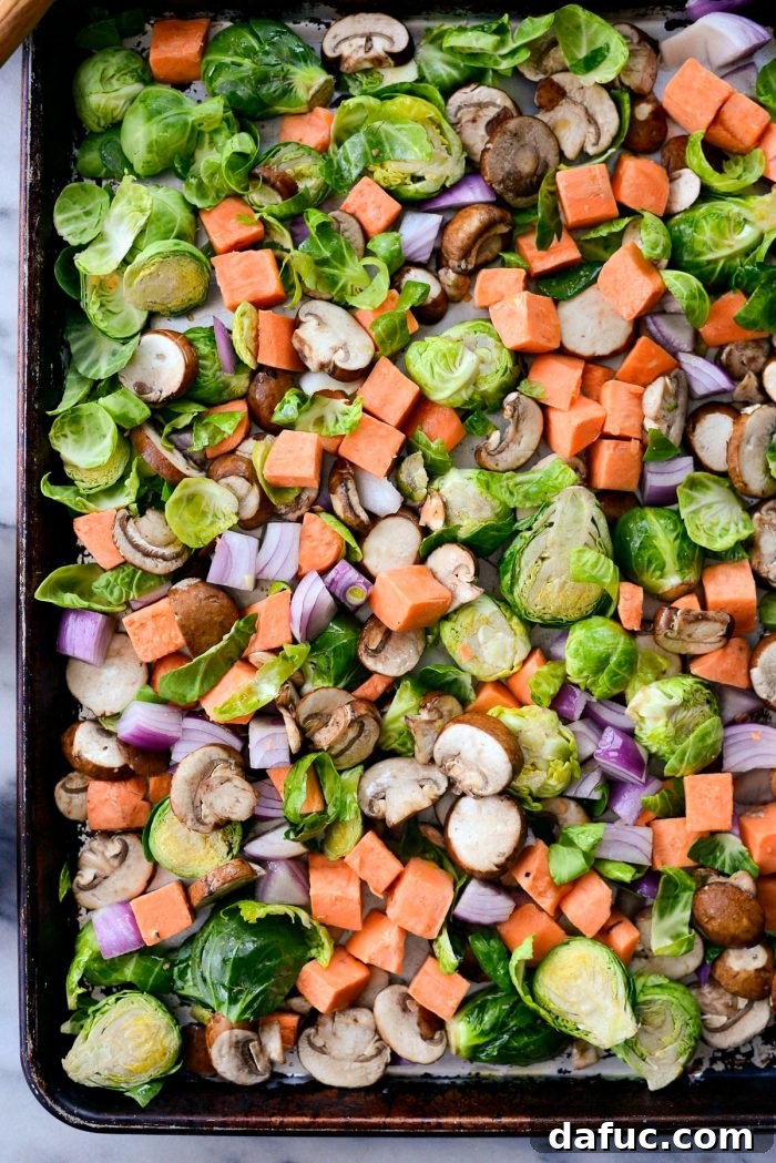 Brussels sprouts, sweet potatoes, red onion, and mushrooms coated in olive oil and seasoning on a sheet pan, ready for roasting. SimplyScratch.com easy breakfast recipe.