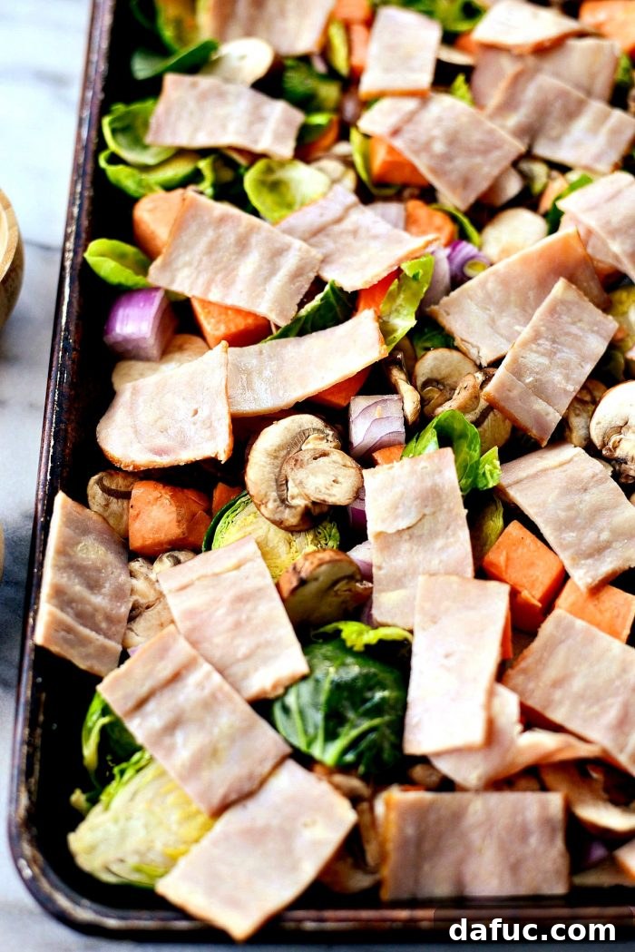 Bacon slices laid over the seasoned vegetables on the sheet pan, ready for the initial roast.