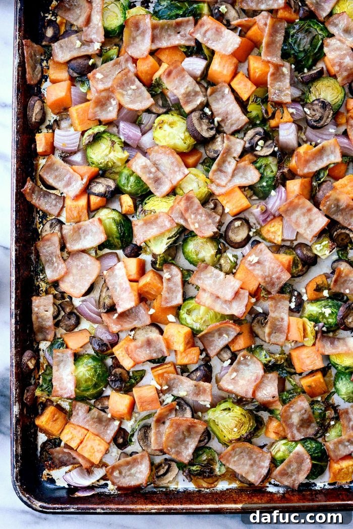 Sheet pan breakfast hash after initial roasting, with garlic sprinkled over the tender vegetables and crispy bacon.