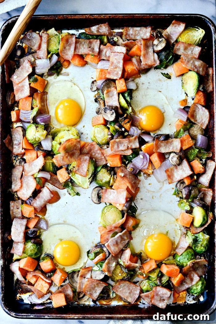 An egg cracked into one of the wells in the sheet pan breakfast hash, illustrating the next step.