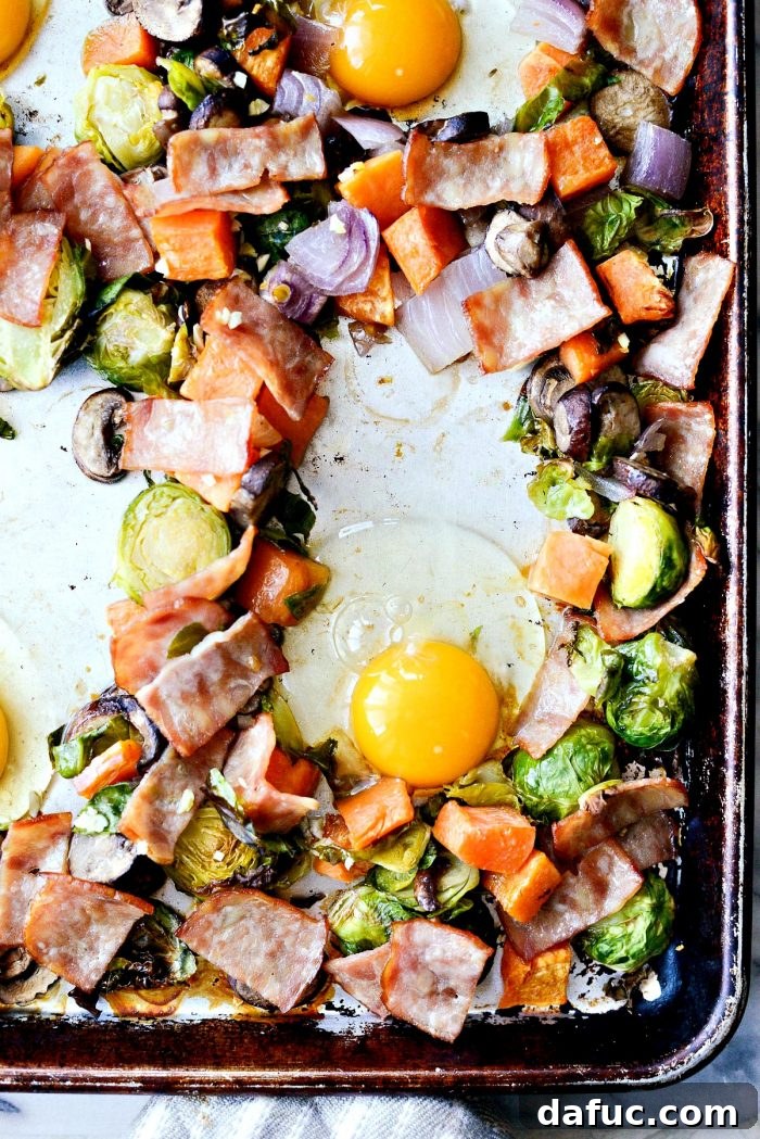 Four eggs cracked into the wells of the sheet pan breakfast hash, baking in the oven for a complete one-pan meal.