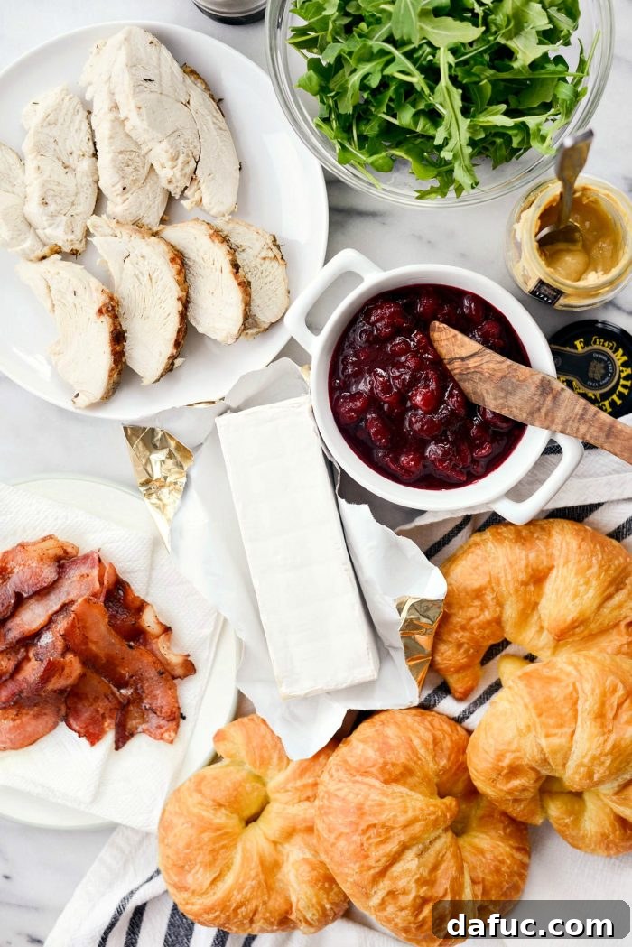 Golden Pressed Turkey Cranberry Croissant 3 Close-up of Croissant Panini ingredients ready to be assembled: turkey slices, crispy bacon, brie cheese, baby arugula, and cranberry spread.