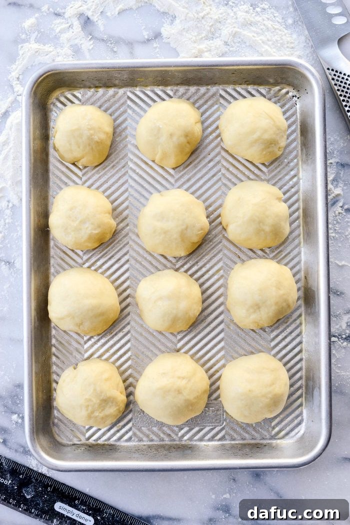 Rolling individual dough pieces into smooth balls for homemade dinner rolls.