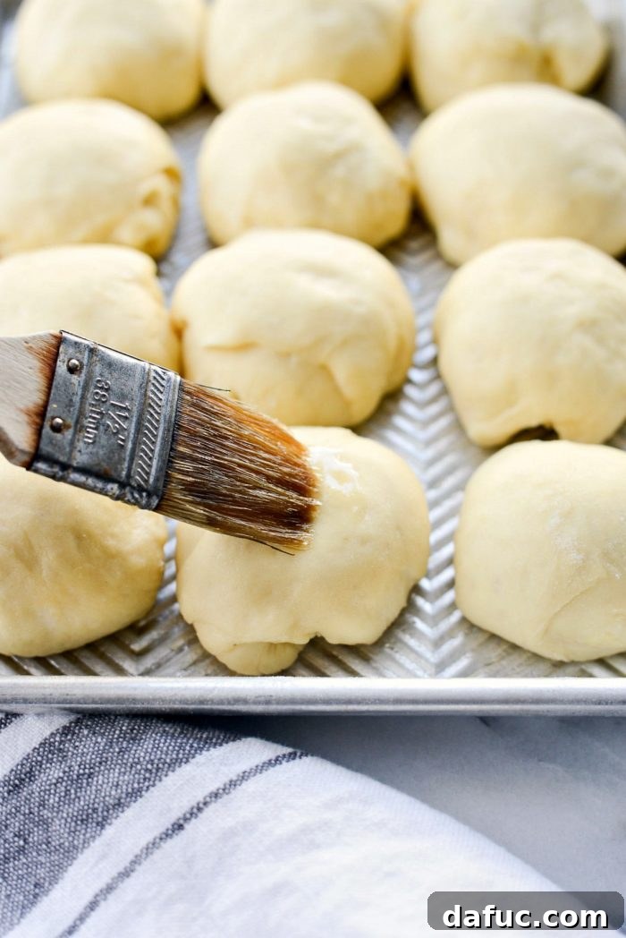 Brushing risen dinner rolls with melted butter before adding rosemary and sea salt.