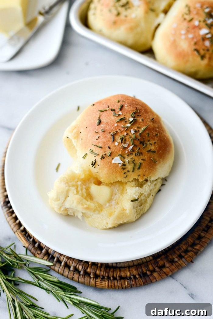 A stack of golden brown Sea Salt Rosemary Dinner Rolls, highlighting their soft texture.