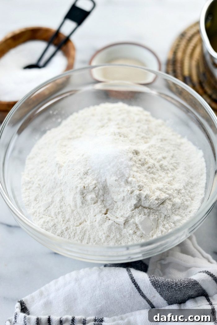Foamy yeast mixture blooming in a stand mixer bowl, a crucial step for soft dinner rolls.