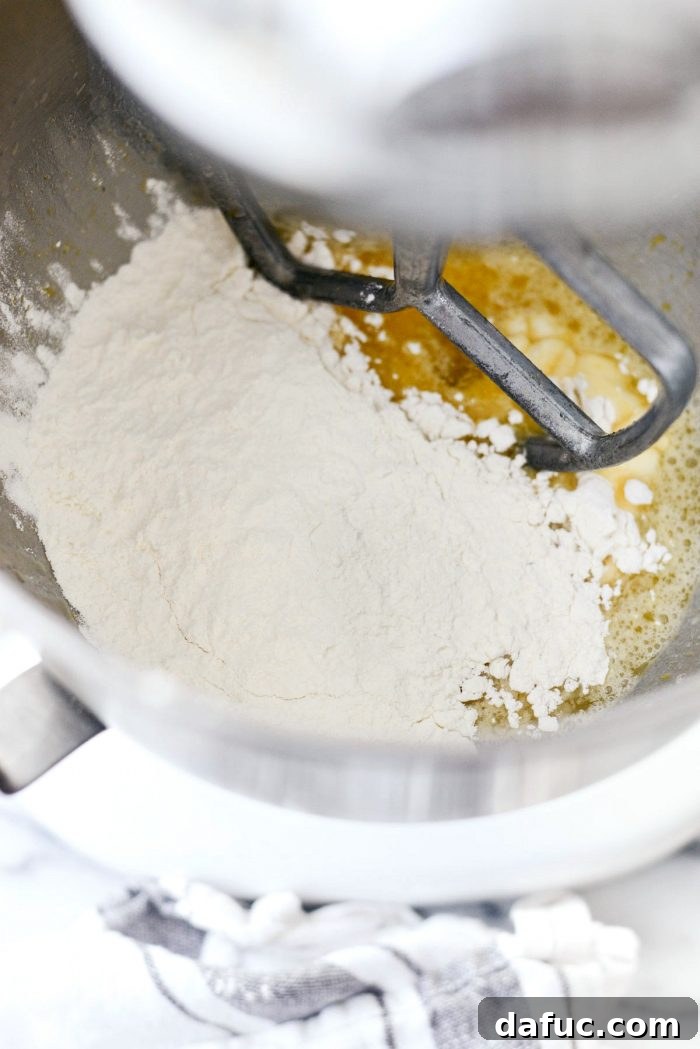 Pouring cooled melted butter into the stand mixer bowl with wet ingredients for dinner rolls.
