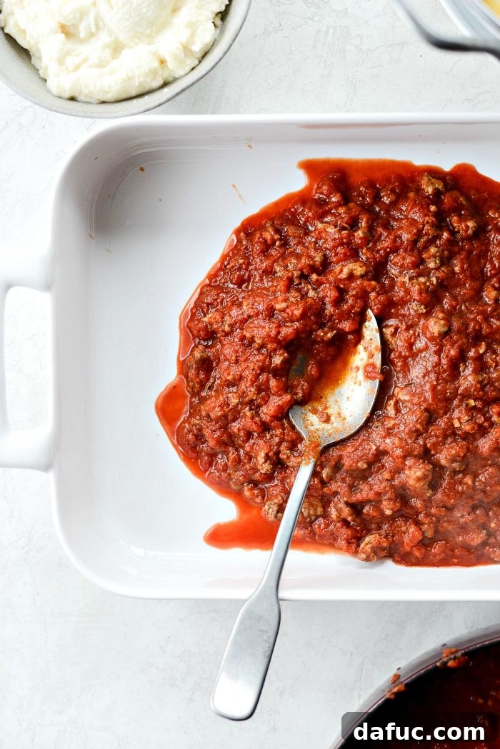 Spreading the first layer of meat sauce in a baking dish