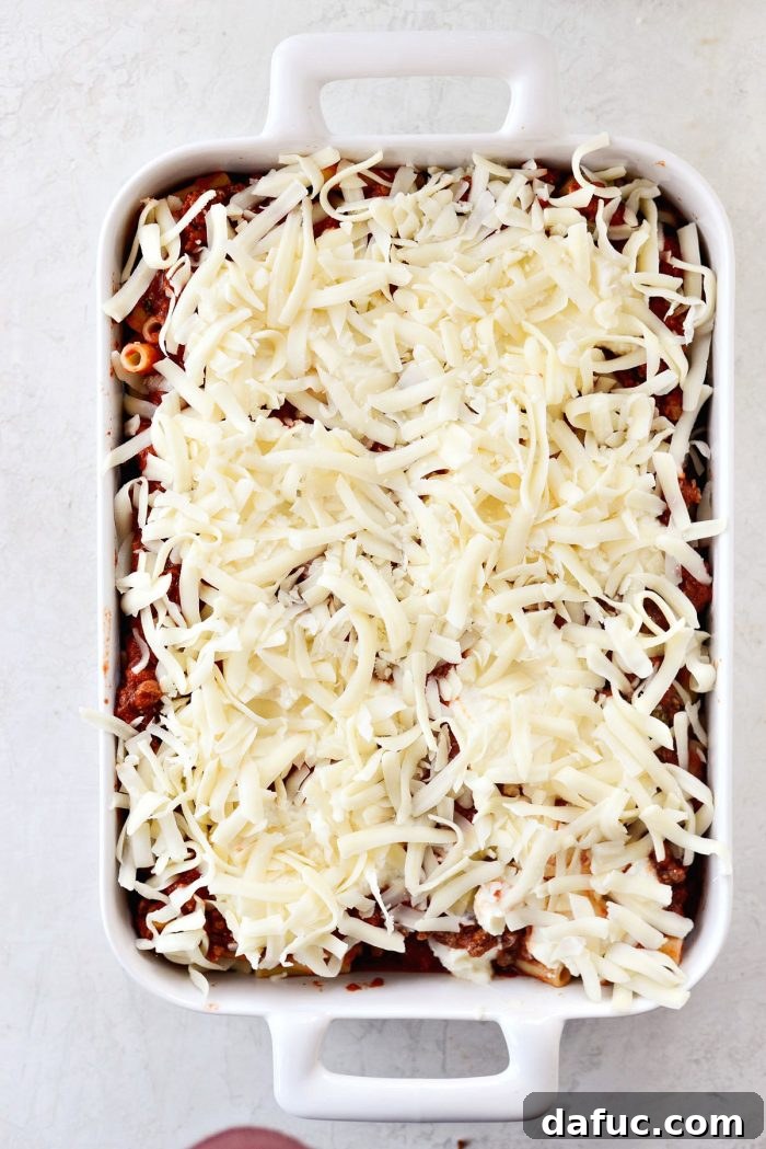 Sprinkling shredded mozzarella cheese on top of baked ziti