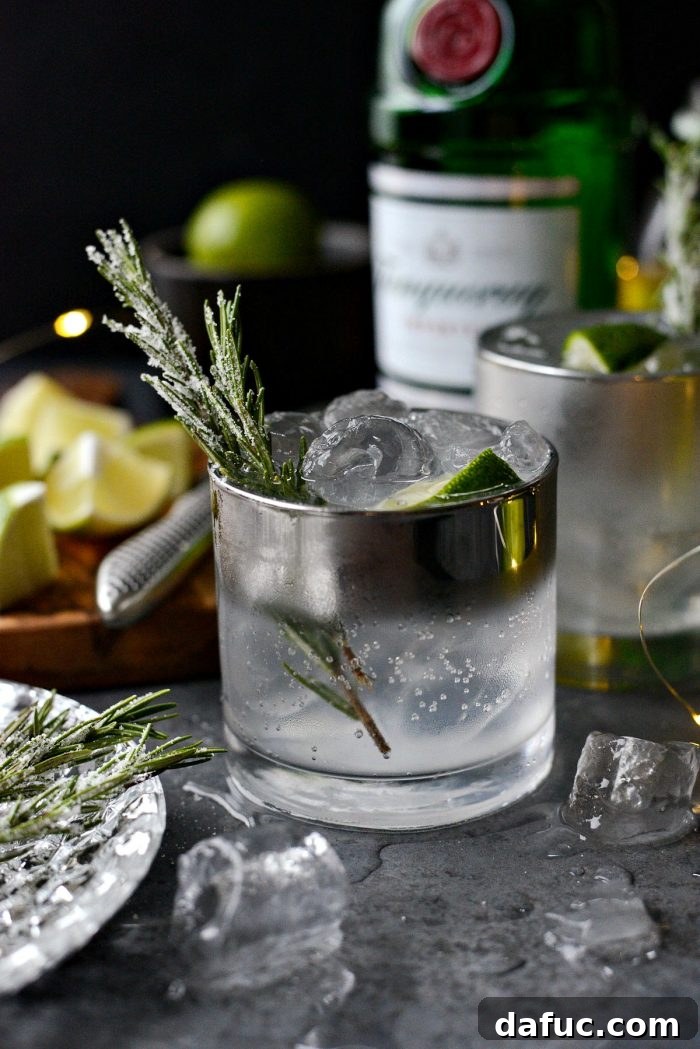 The Perfect Gin and Tonic 2 Classic Gin and Tonic garnished with sugared rosemary and lime, capturing a festive and refreshing holiday drink. The drink is in a clear glass with ice.