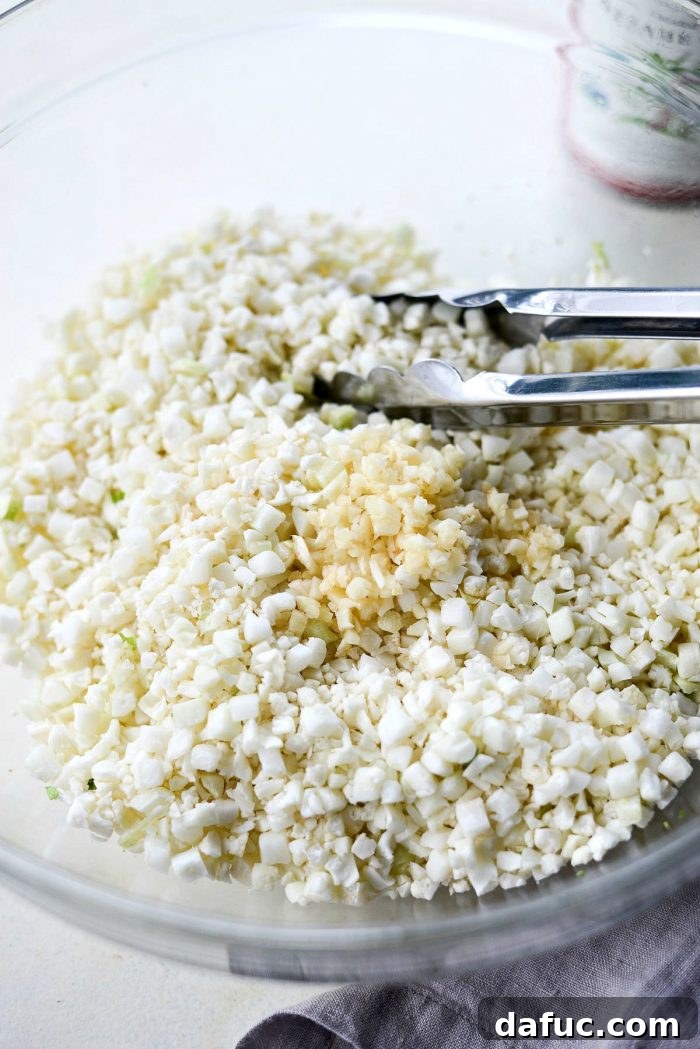Cauliflower rice mixed with minced garlic and sesame oil in a bowl, ready to be added to the sheet pan.