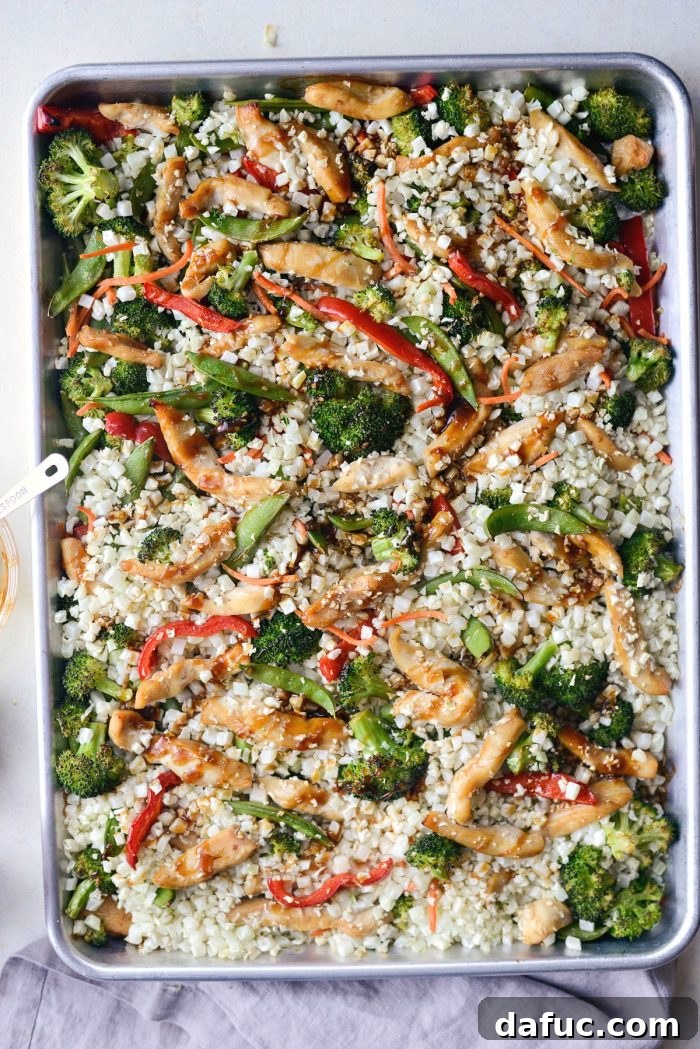 Cauliflower rice added to the sheet pan with chicken and vegetables, gently tossed and ready for final roasting.