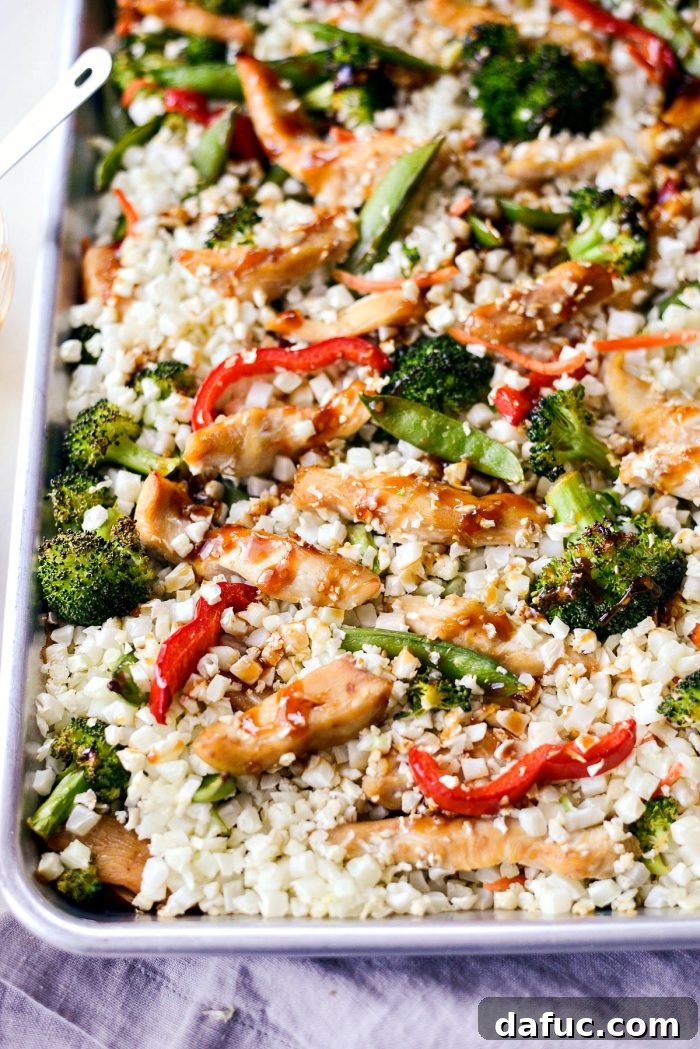 Sheet pan with teriyaki chicken, vegetables, and cauliflower rice, glistening with sauce after broiling.