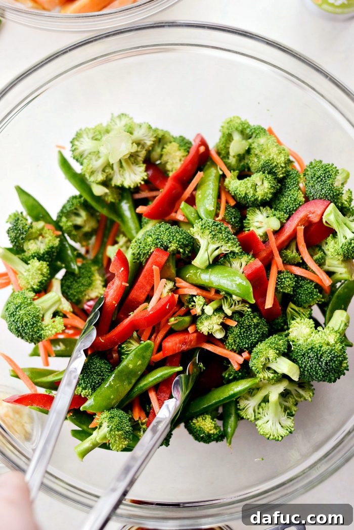 Mixed vegetables including broccoli, sugar snap peas, carrots, and red bell pepper in a large mixing bowl.