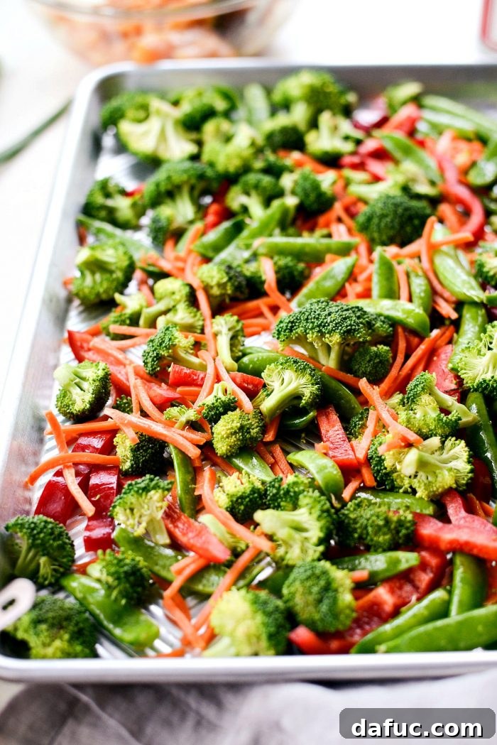 Tossing mixed vegetables with toasted sesame oil in a bowl, ready for roasting.