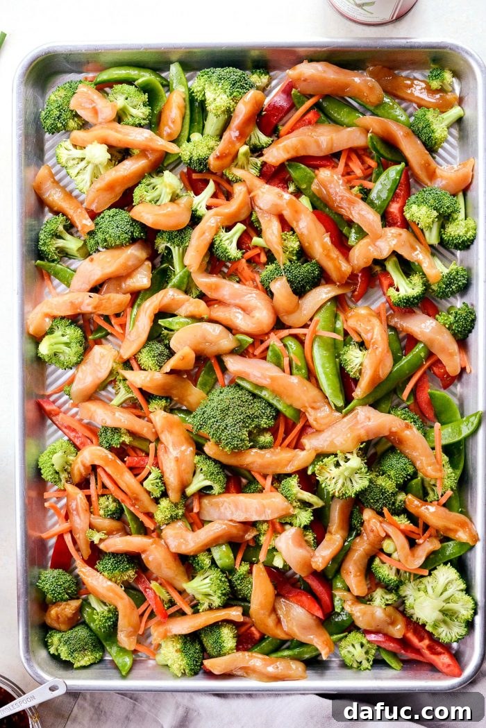 Hot sheet pan with seasoned vegetables and marinated teriyaki chicken, ready for the oven.