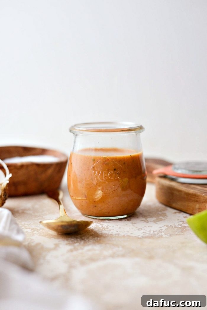 Sweet Heat Chipotle Vinaigrette 7 A serving spoon lifting creamy Chipotle Honey Vinaigrette from a jar, highlighting its rich color and texture.
