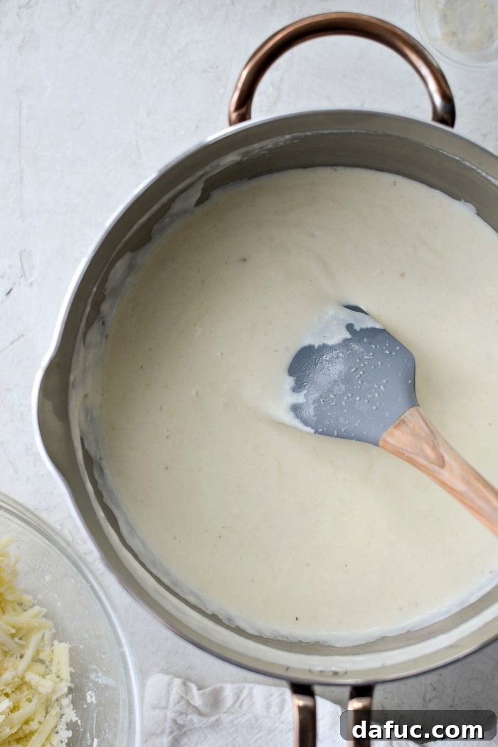 Opulent Lobster Mac and Cheese 13 Adding grated cheese to the thickened cream sauce in a saucepan.