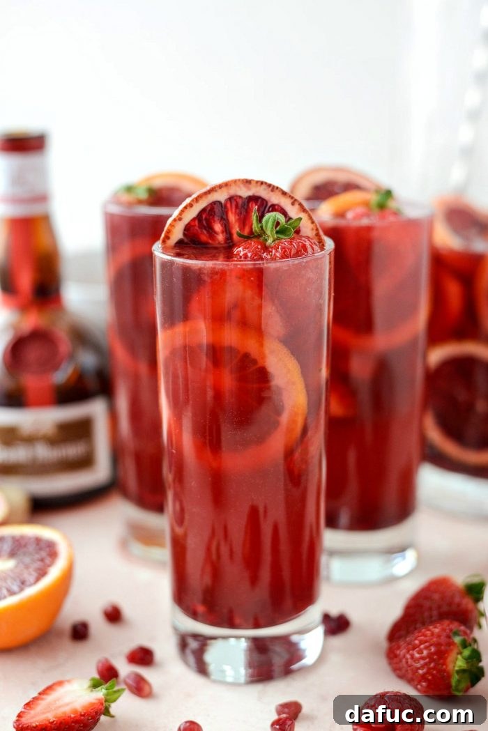 Pouring Champagne Sangria into glasses, each pre-filled with fresh pomegranate arils and raspberries, enhancing the presentation and flavor.