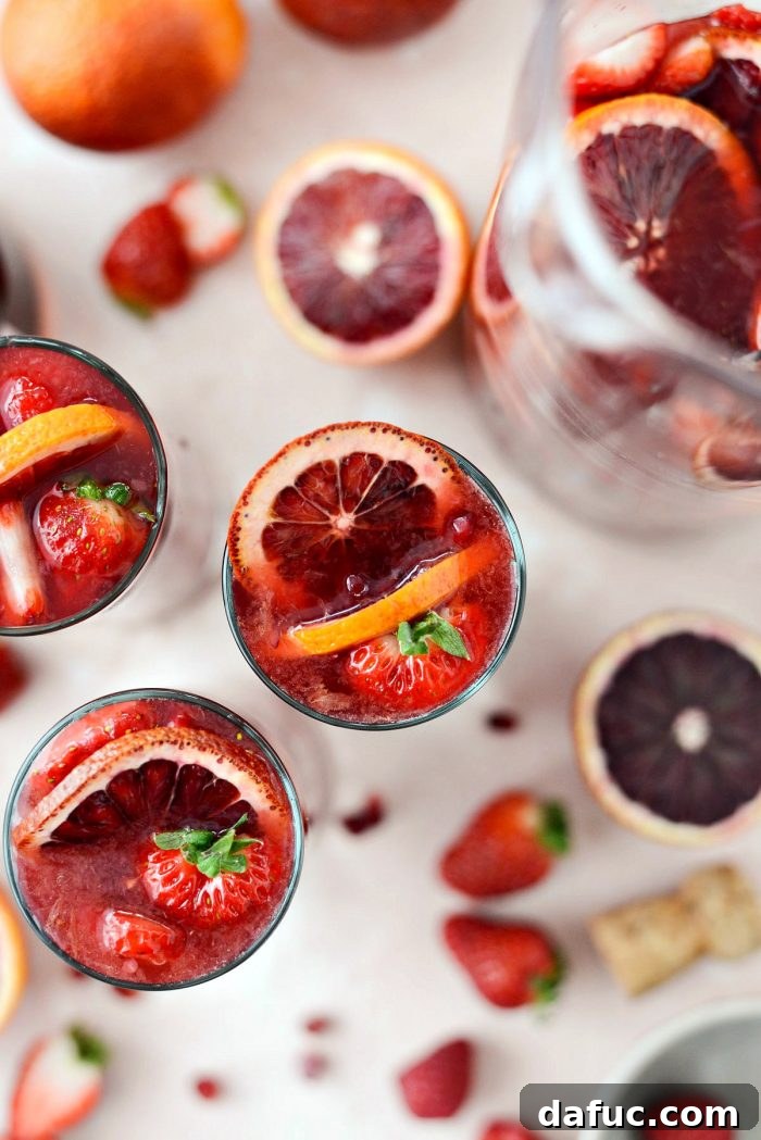 Close-up of a pitcher of Champagne Sangria, showcasing the vibrant red color and an abundance of fresh fruit like strawberries, raspberries, and blood orange slices.