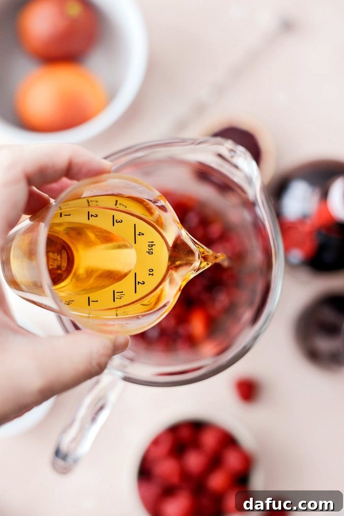 Adding Grand Marnier liqueur to the fruit and juice mixture in the pitcher for Champagne Sangria.