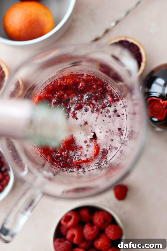 Pouring a bottle of chilled Brut Rosé Champagne into the pitcher of sangria ingredients.