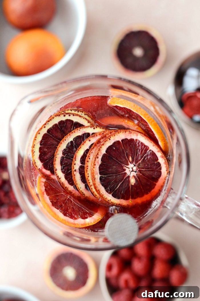 Champagne Sangria in a pitcher with blood orange slices and raspberries on top, ready to be gently stirred.