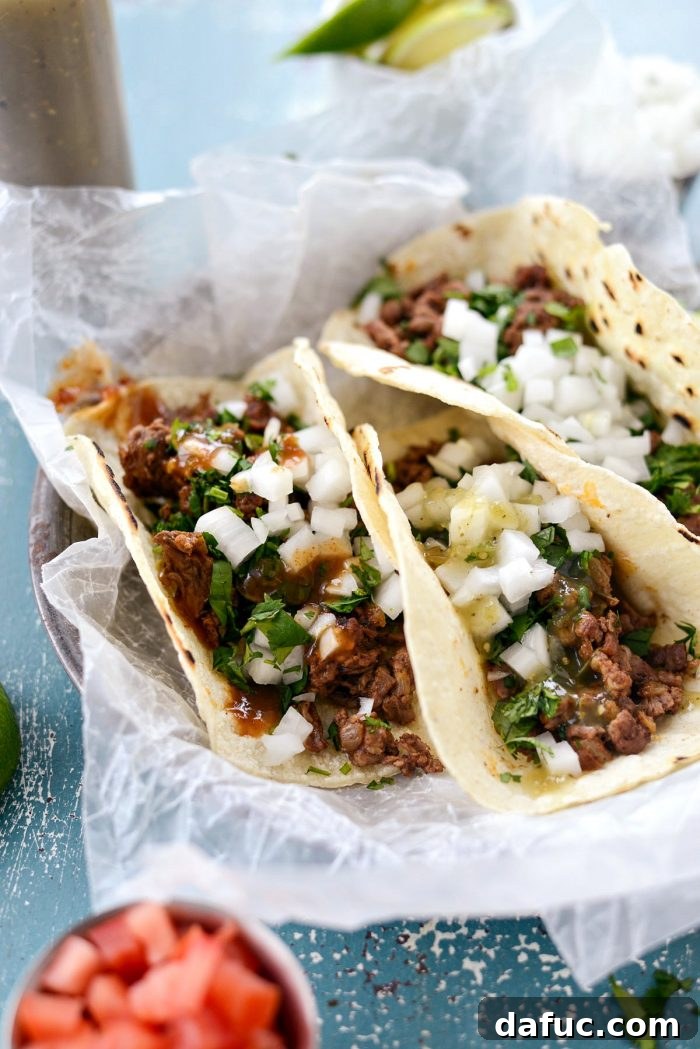 Close-up of freshly made Easy Beef Street Tacos, highlighting the seasoned skirt steak, white onion, and cilantro on toasted corn tortillas. SimplyScratch.com recipe.