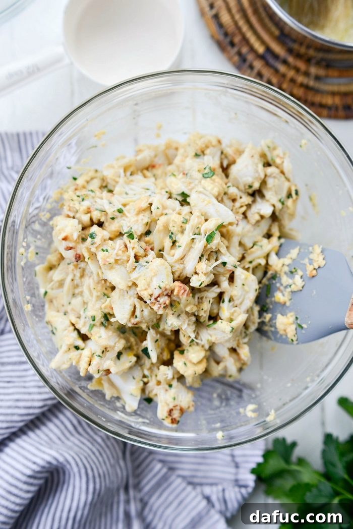 Golden Baked Maryland Crab Delights 12 A rubber spatula gently mixing crab meat and binder in a bowl.