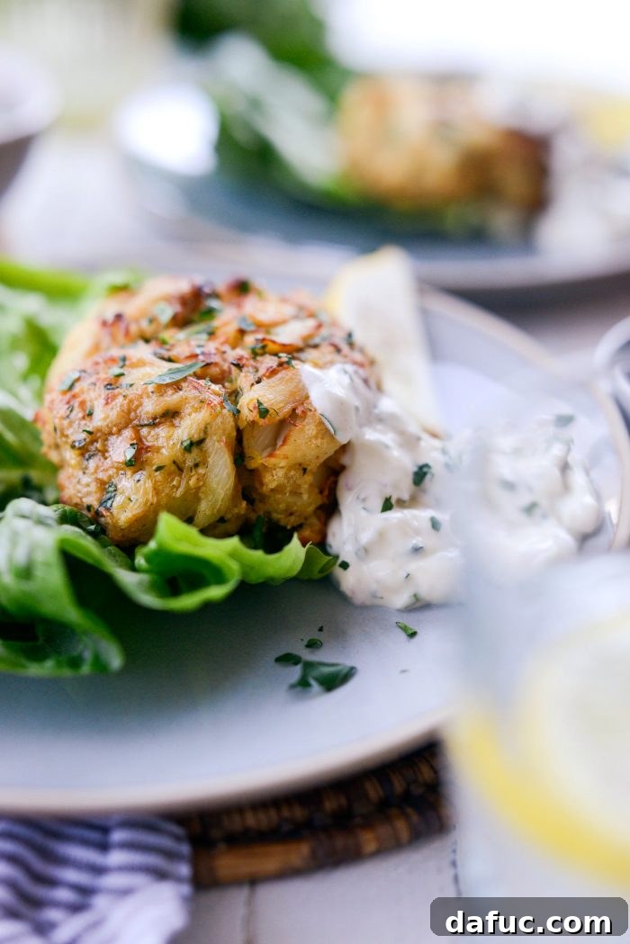Golden Baked Maryland Crab Delights 20 A beautifully arranged plate with two crispy baked Maryland crab cakes, tartar sauce, lemon, and fresh herbs.