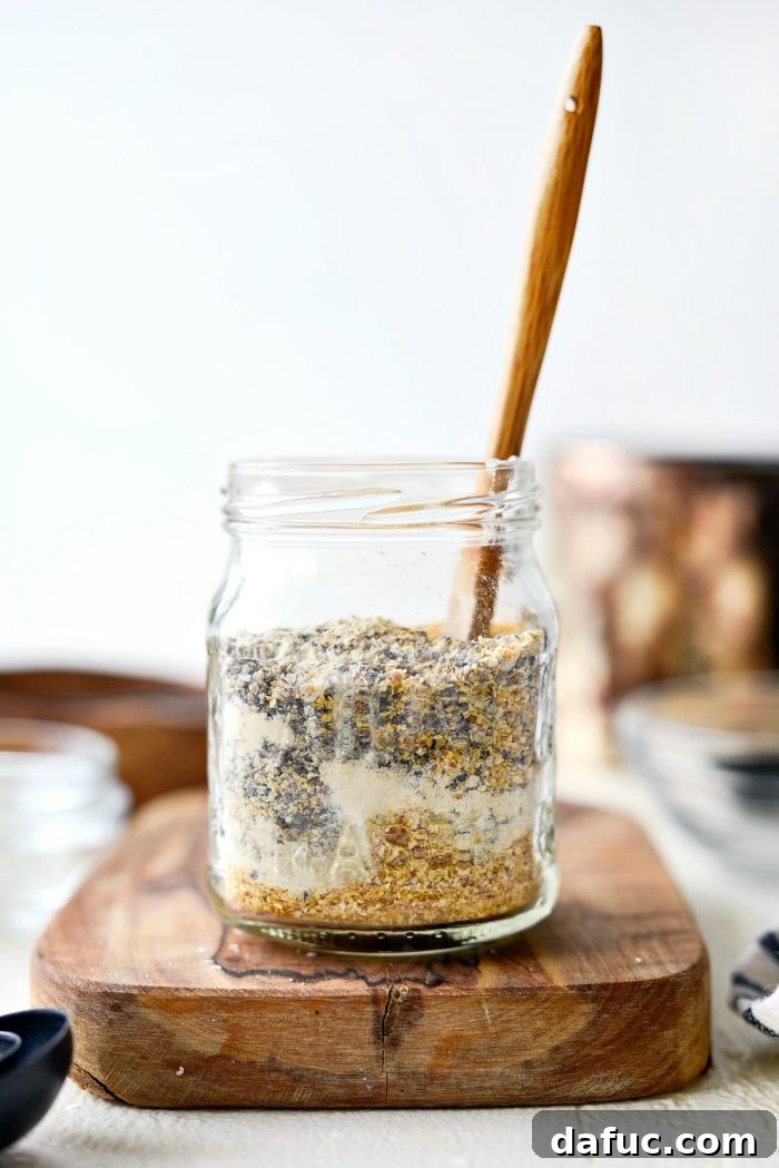 A hand stirring the Homemade Lemon Pepper Seasoning mixture in a glass bowl with a spoon.