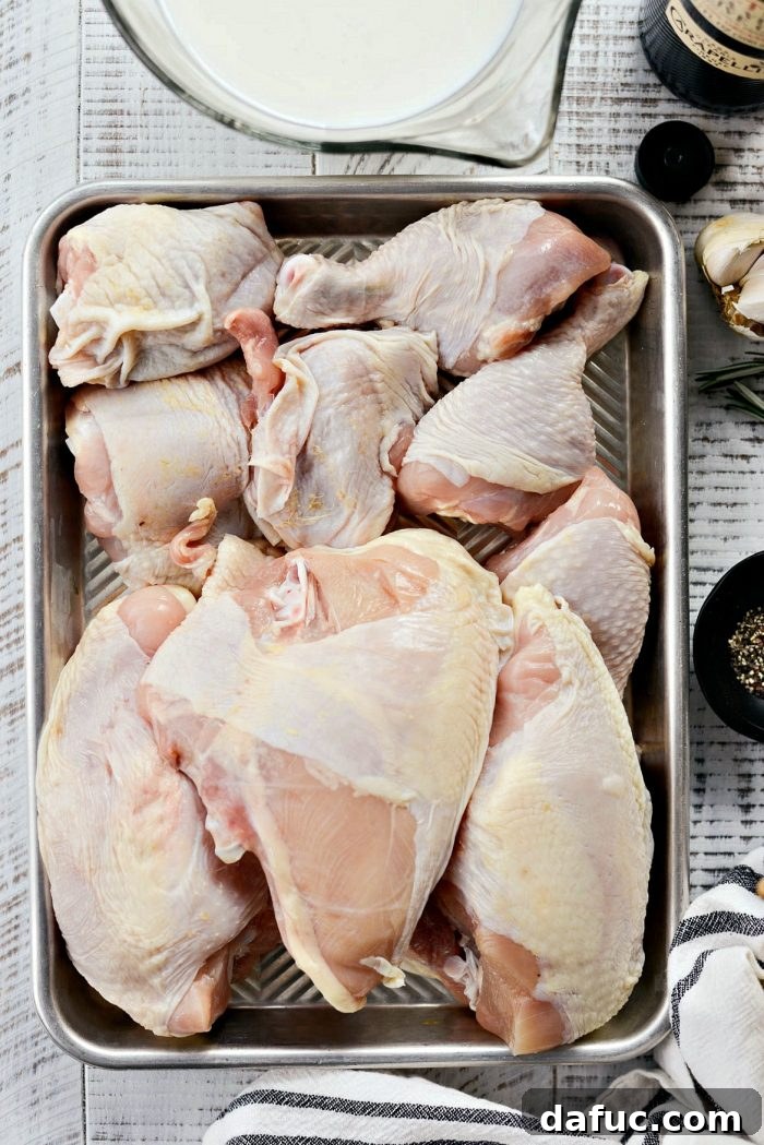 A bowl of fresh ingredients for the buttermilk chicken marinade, including garlic cloves, rosemary sprigs, and a bottle of buttermilk.