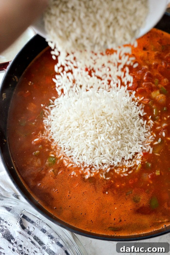 Effortless One Pot Jambalaya 17 Stirring long grain white rice into the boiling Jambalaya broth | SimplyScratch.com #skillet #shrimp #andouille #rice #creole #chicken #homemade