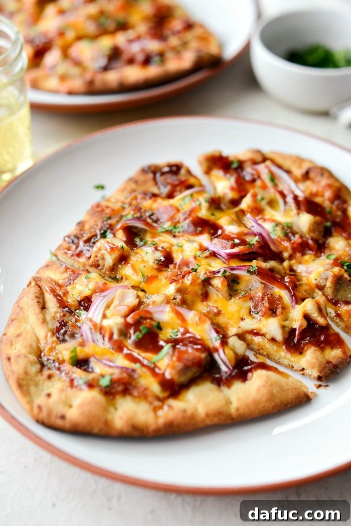 Close-up of BBQ Chicken Naan Pizza ingredients on a baking sheet before going into the oven. Features chicken, red onion, cheese, and barbecue sauce on naan bread.