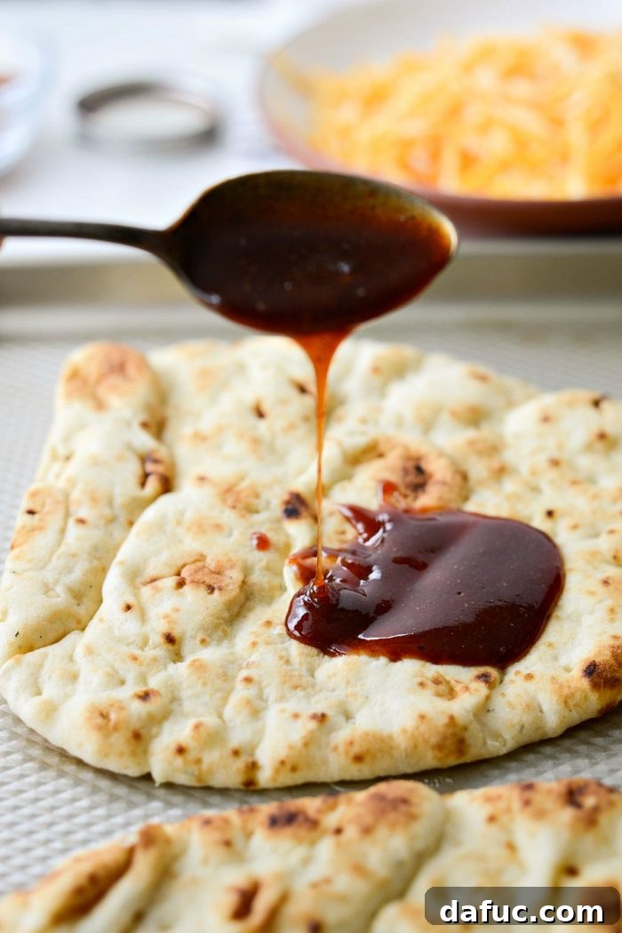 Various ingredients for BBQ Chicken Naan Pizzas laid out: naan bread, cooked chicken, red onion, cheese, and barbecue sauce.
