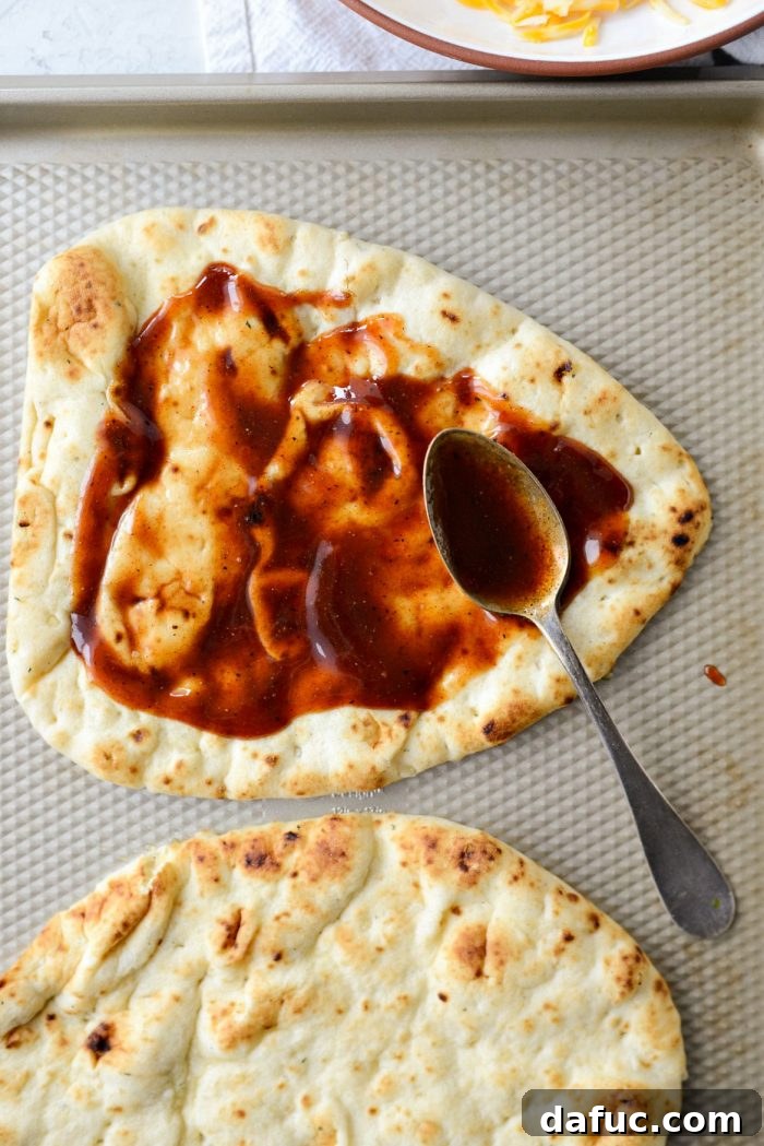 Applying sweet barbecue sauce evenly onto naan bread, leaving a border for the crust.