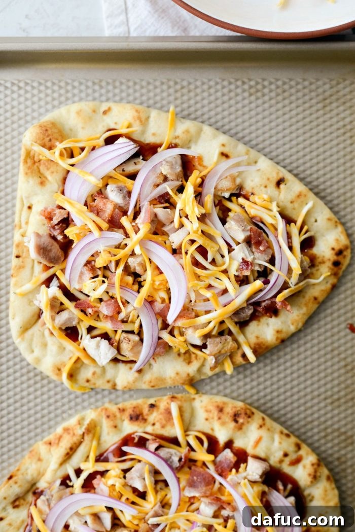 Topping naan pizzas with chicken, bacon, red onion, and extra cheese, ready for the oven.
