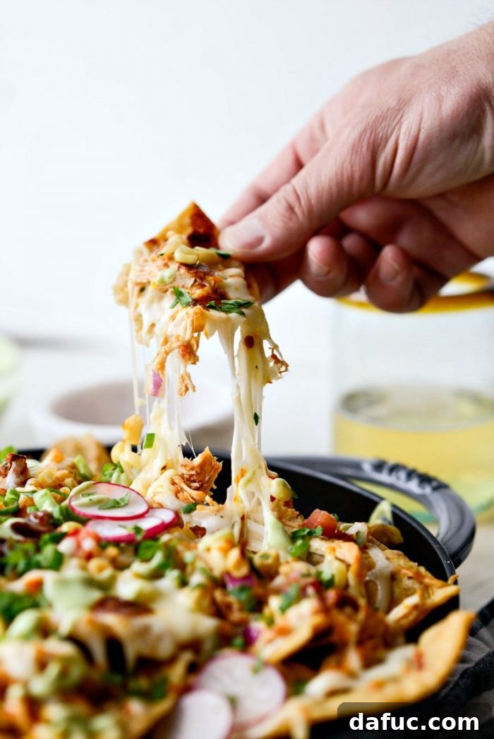 Golden Lava Chicken Nachos 12 A hand reaching for a chip from a platter of fully loaded Jacuzzi Chicken Nachos, highlighting the tempting cheese pull and vibrant toppings.