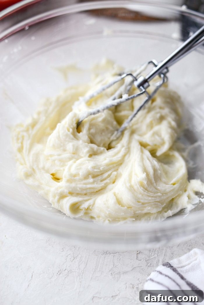 A clear mixing bowl containing a smooth mixture of cream cheese, sugar, and vanilla extract, ready for the whipped cream.