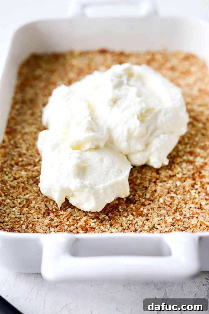 A generous amount of creamy whipped cream cheese filling spread evenly over the cooled pretzel crust in a baking dish.