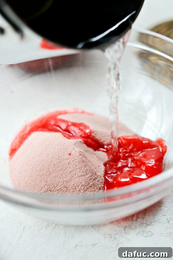 Boiling water being carefully added to a bowl of strawberry Jell-O mix, initiating the dissolution process.