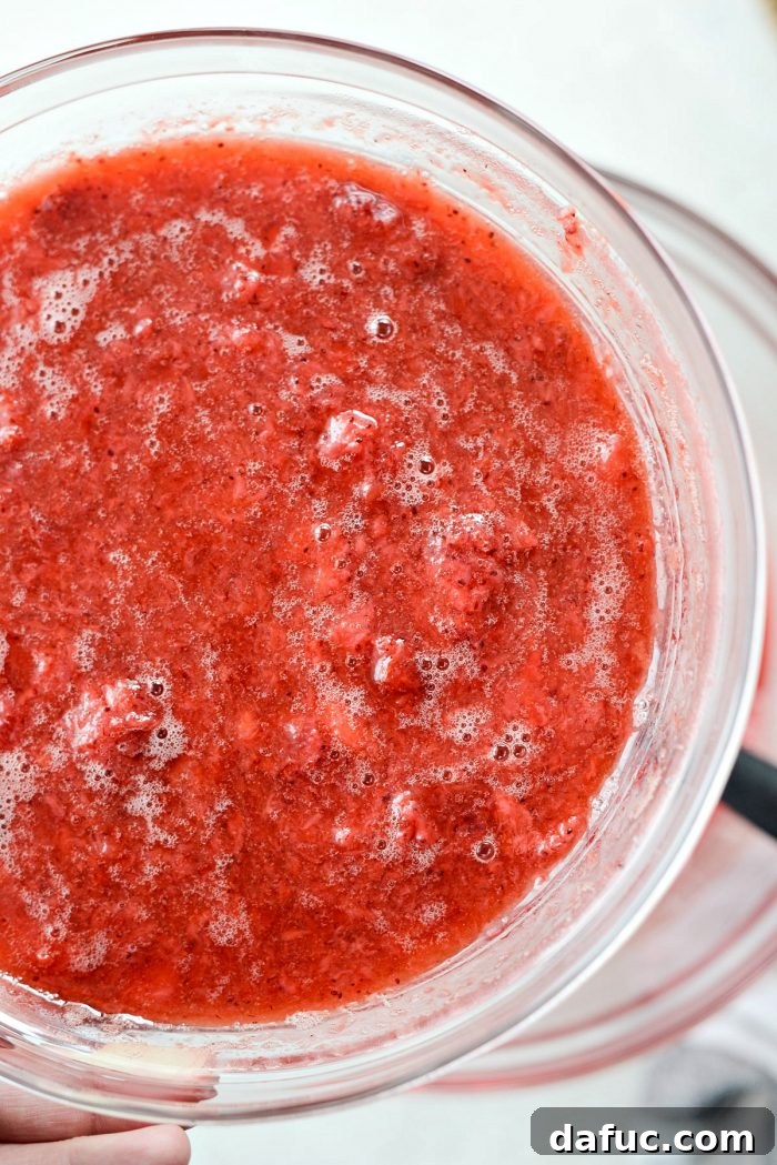 Thawed sliced strawberries being added to the prepared Jell-O mixture, infusing it with real fruit.