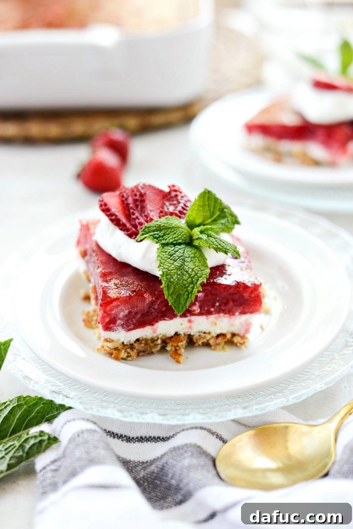 A close-up shot of a single strawberry pretzel dessert bar, showing off its distinct and vibrant layers of crust, cream, and jello.