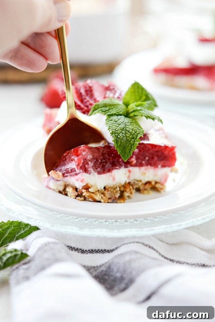 A gold spoon cutting into the soft layers of a strawberry pretzel dessert bar, highlighting its texture.
