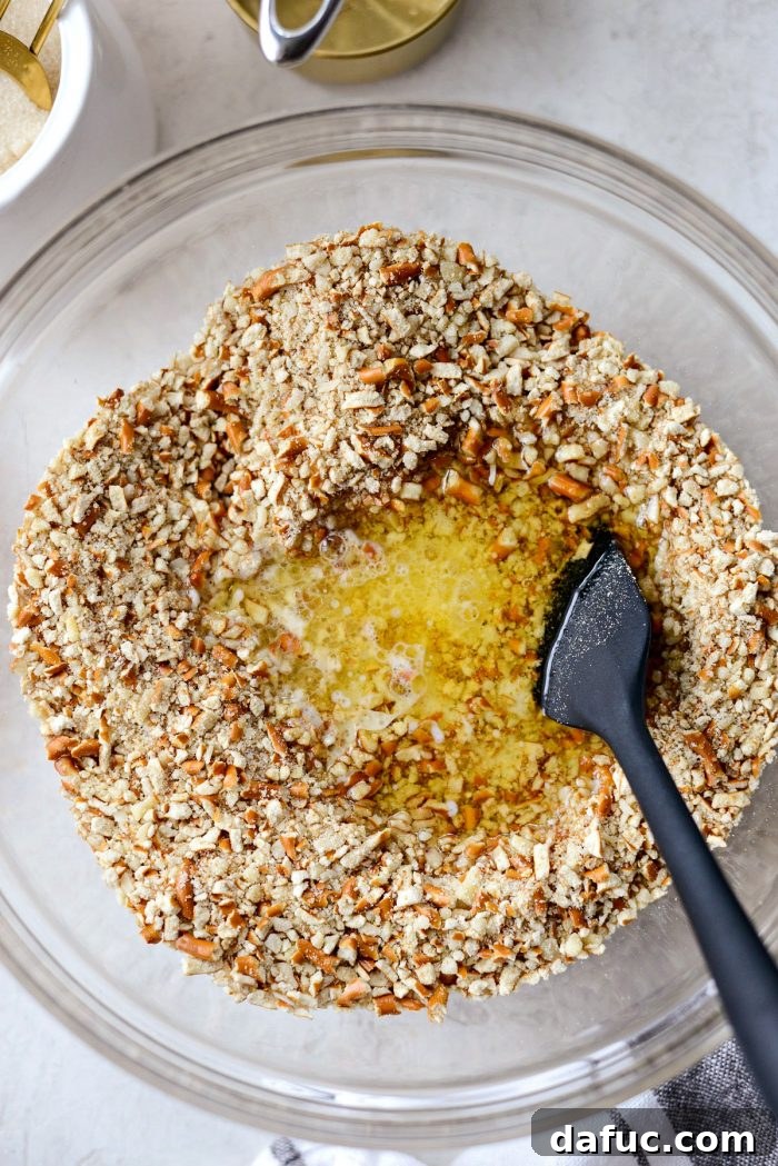 Pouring melted unsalted butter into the bowl containing the pretzel and almond mixture, creating the crust base.