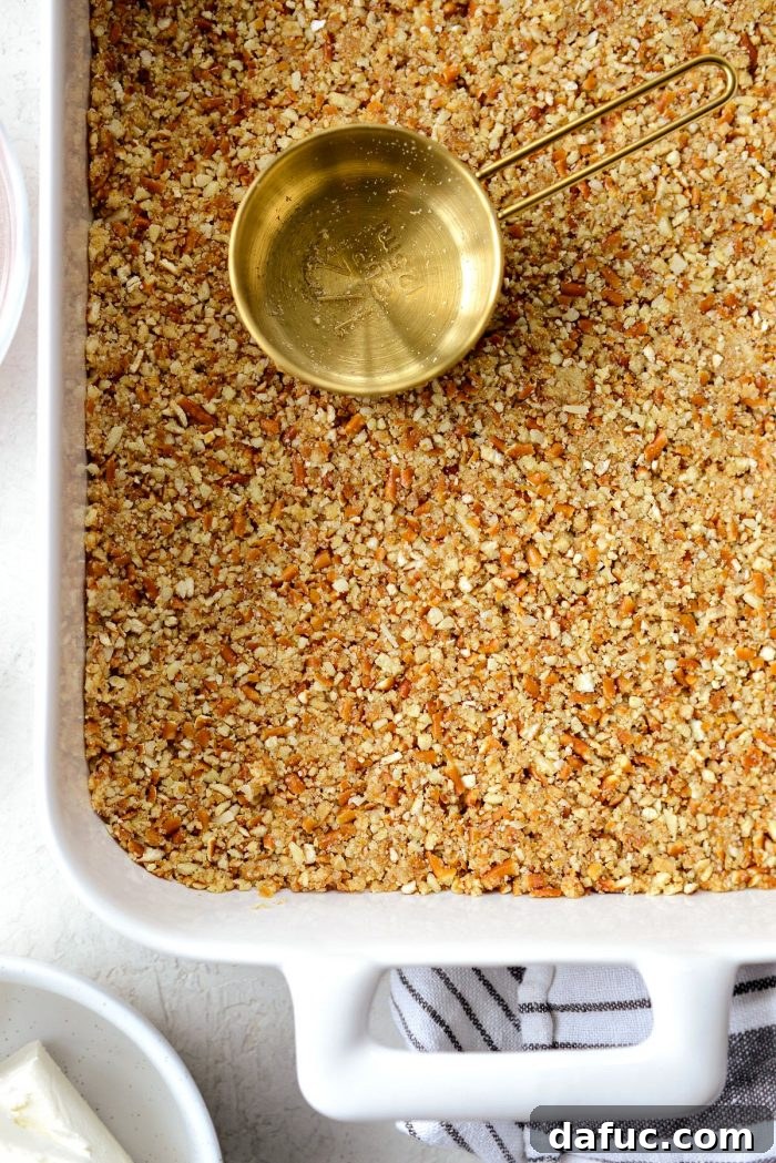 The crust mixture firmly pressed into the white baking pan using a gold measuring cup, ensuring an even and compact base.