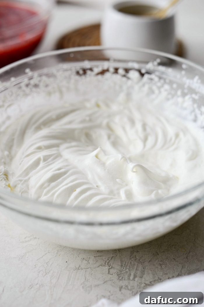 A clear mixing bowl holding perfectly whipped unsweetened heavy cream, forming stiff peaks.